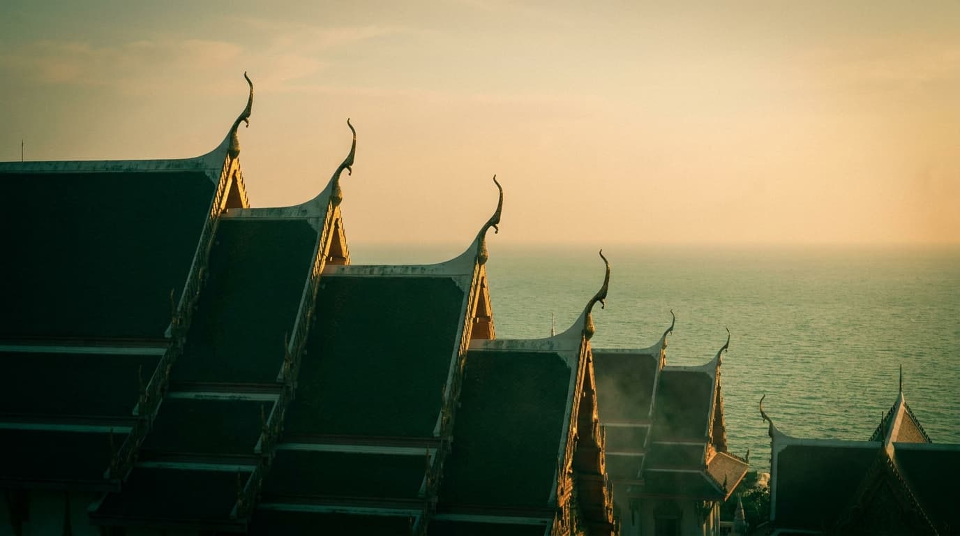 Thailändische Tempeldächer mit Chofa-Giebelspitzen vor dem ruhigen Meer